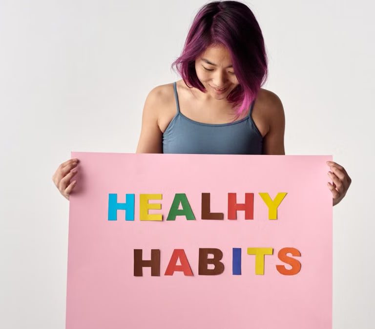 Asian woman holding a colorful 'Healthy Habits' sign in a studio setting, promoting wellness.