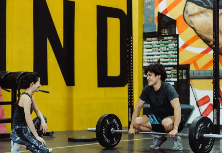 Two young adults in a gym participating in a weightlifting session, sharing a positive moment.